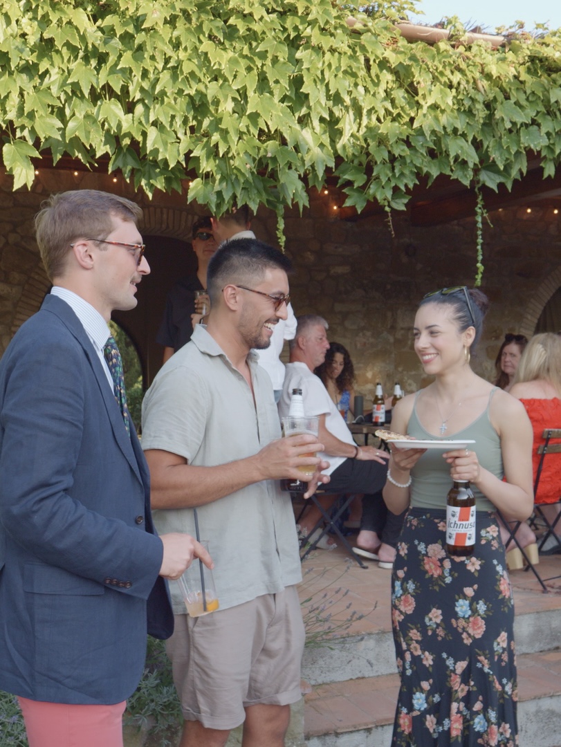 Guests chatting with pizza and drinks under a vine-covered terrace