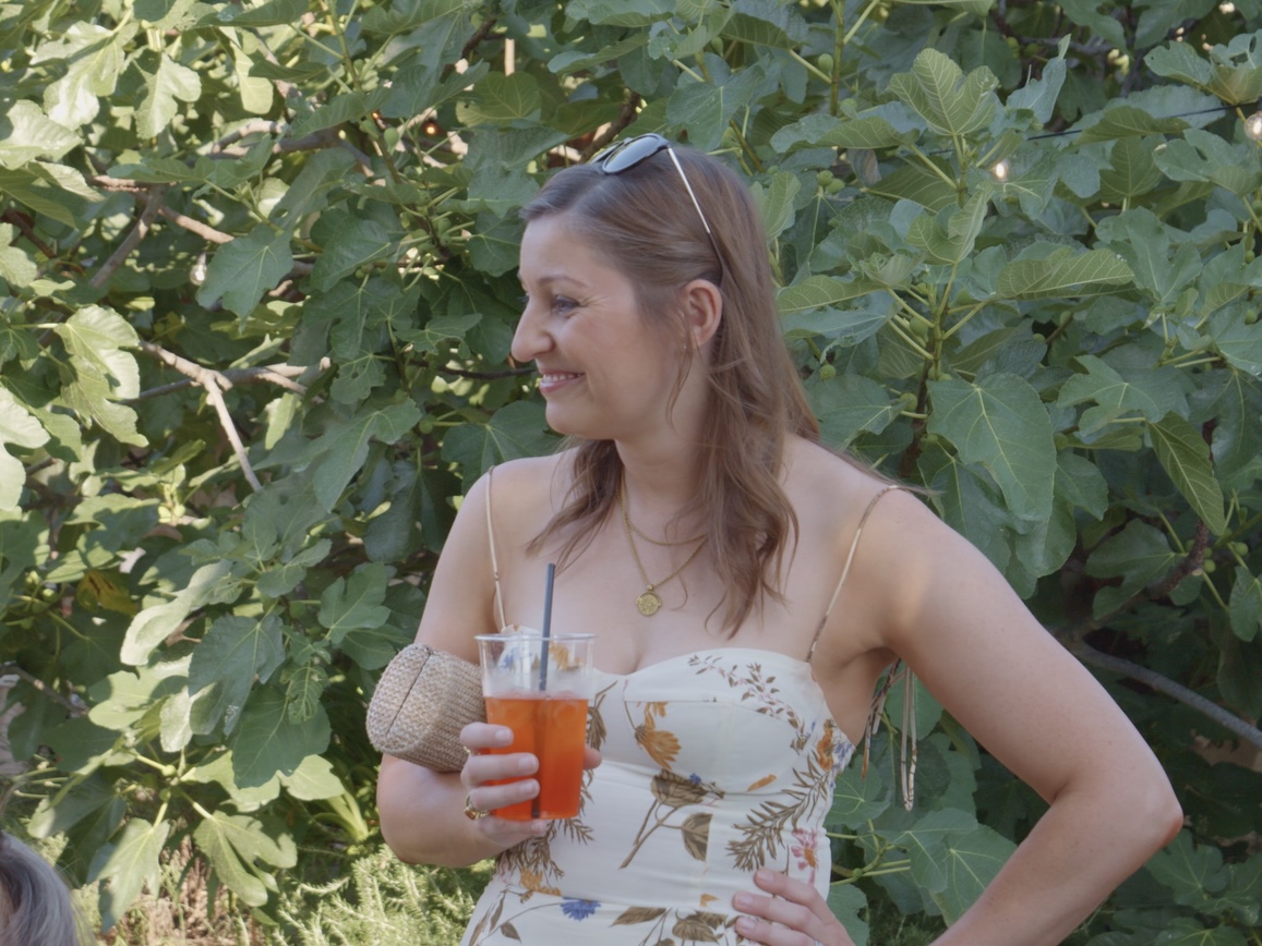 A guest smiling with a spritz under the fig trees