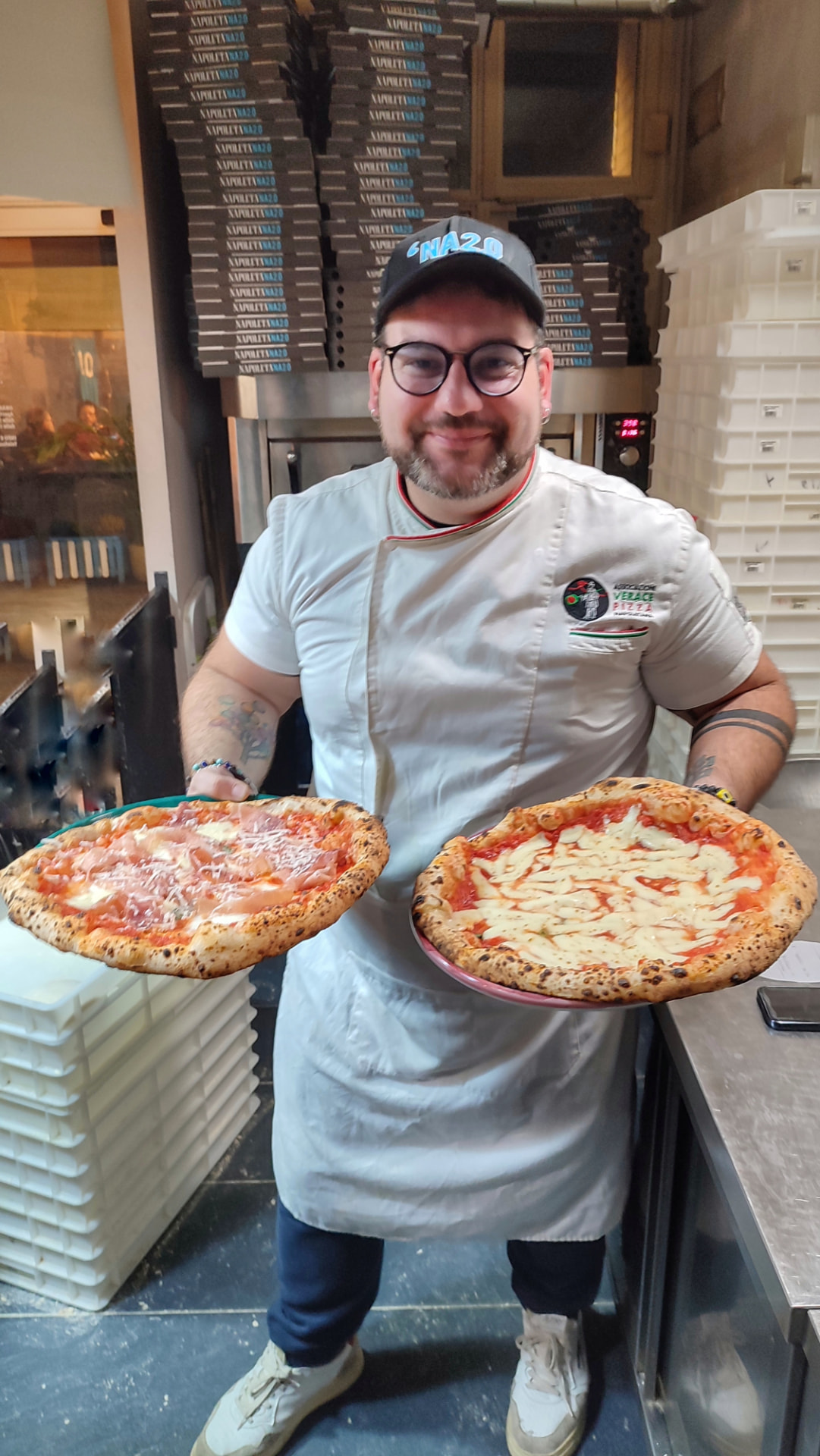 Our Neapolitan pizzaiolo in the kitchen of La Napoletana 2.0 in Siena, holding two freshly baked pizzas